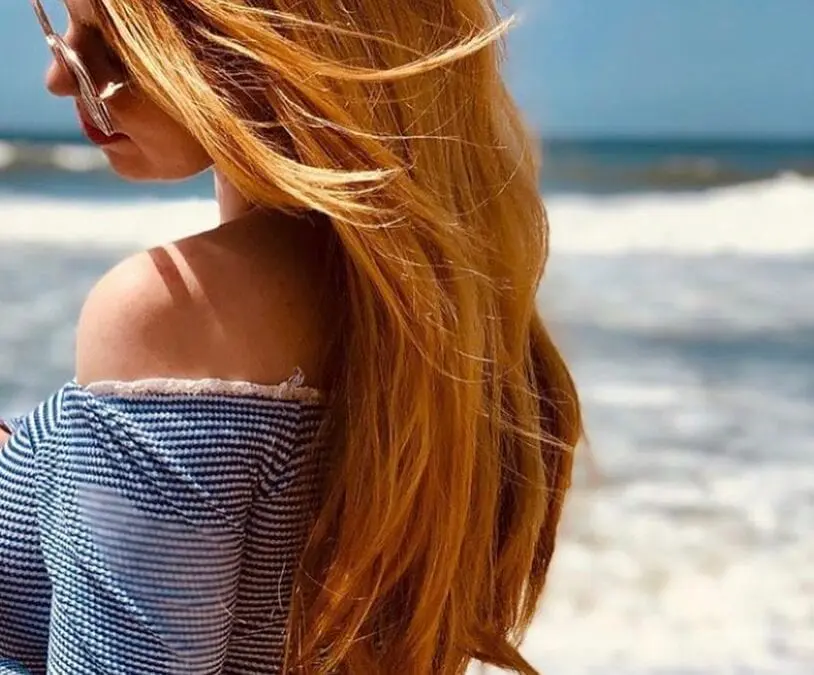 Profile view of a woman at the beach with ultra-long, windblown hair featuring a vibrant custom copper red hair color by Lisa Edwards at Sunday Salon in Raleigh, NC.