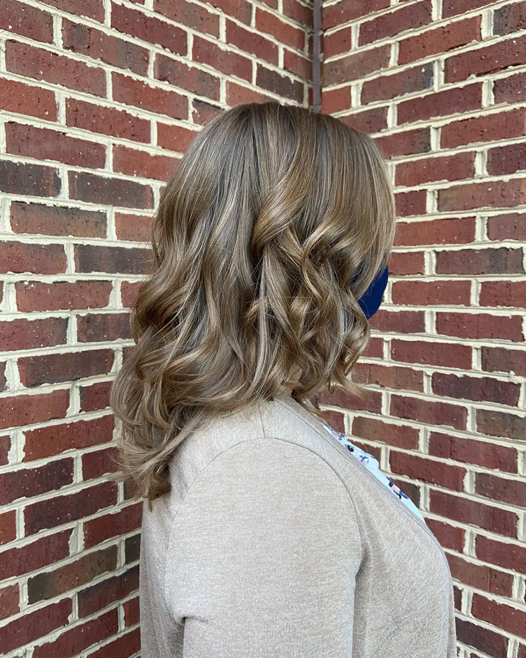 Side view of a woman with medium-length hair featuring dimensional caramel bronde highlights and voluminous, polished curls, created at Sunday Salon in Raleigh, NC.