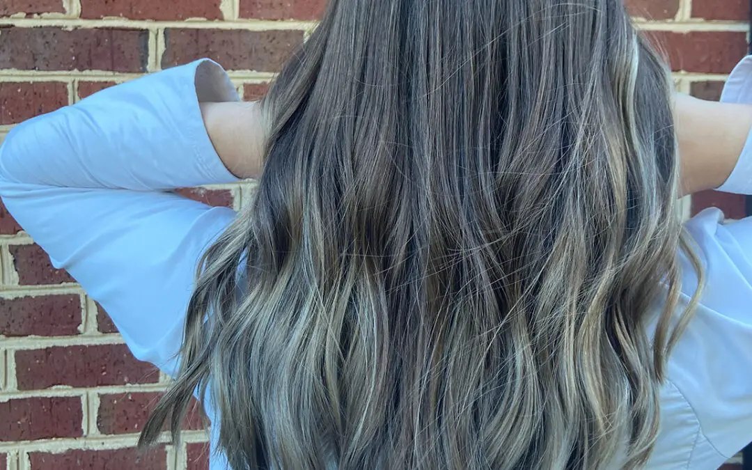Back view of long, thick hair with cool ash blonde highlights over a deep brunette base, styled in loose beachy waves at Sunday Salon in Raleigh, NC.