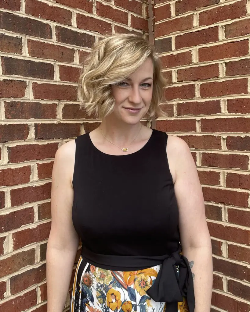 Woman with a chin-length textured bob styled in deep side-parted waves, featuring bright vanilla blonde highlights and a soft shadow root, styled at Sunday Salon in Raleigh, NC.