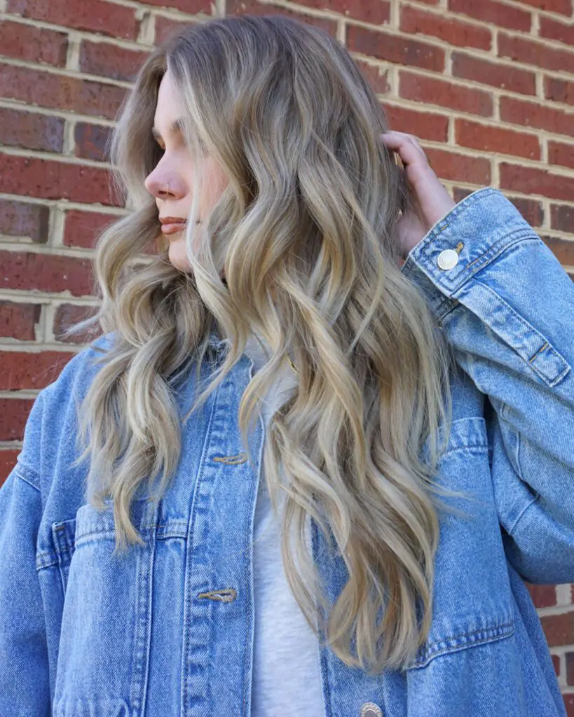 Dimensional Ash Blonde Balayage with Long Lived-In Waves Woman looking to the side showcasing ultra-long lived-in ash blonde balayage, bright face-framing highlights, and loose beachy waves, customized by Lisa Edwards at Sunday Salon in Raleigh, NC.
