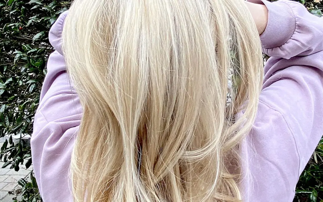 Back view of medium-long, voluminous hair styled in a bouncy layered blowout featuring an ultra-bright, creamy platinum blonde color crafted at Sunday Salon in Raleigh, NC.
