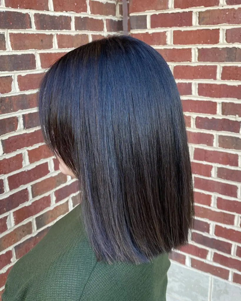 Side profile of a woman with a sleek, straight blunt collarbone-length lob featuring a high-shine midnight brunette color, styled at Sunday Salon in Raleigh, NC.