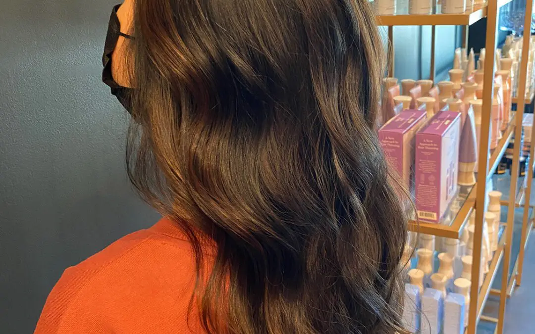 Side profile of a woman with ultra-long, thick espresso brown hair styled in soft cascading waves with subtle chestnut babylights, inside Sunday Salon in Raleigh, NC.