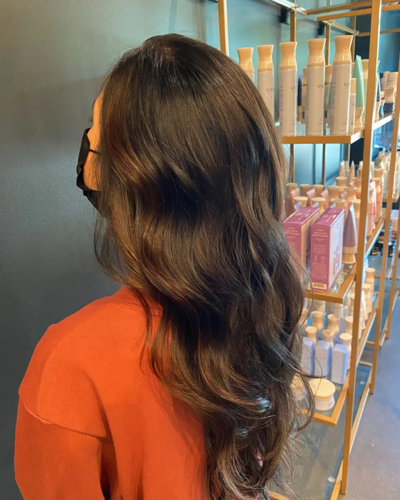 Dimensional Espresso Brunette with Subtle Chestnut Babylights Side profile of a woman with ultra-long, thick espresso brown hair styled in soft cascading waves with subtle chestnut babylights, inside Sunday Salon in Raleigh, NC.