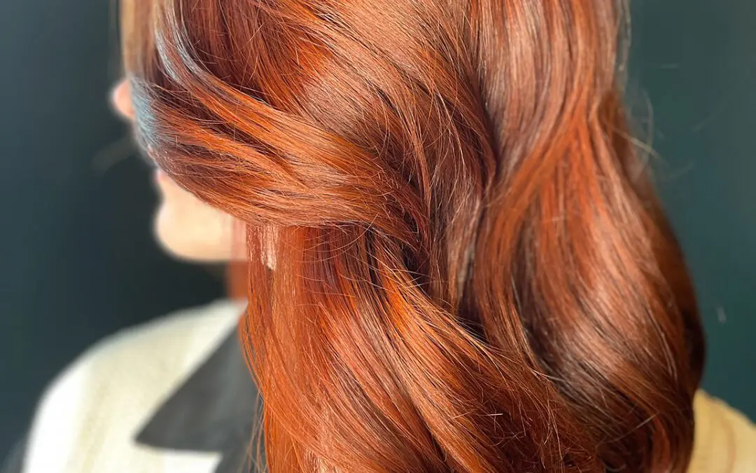 Side view of a woman with medium-long hair featuring a dimensional fiery copper and auburn balayage styled in soft sweeping waves, customized by Lisa Edwards at Sunday Salon in Raleigh, NC.