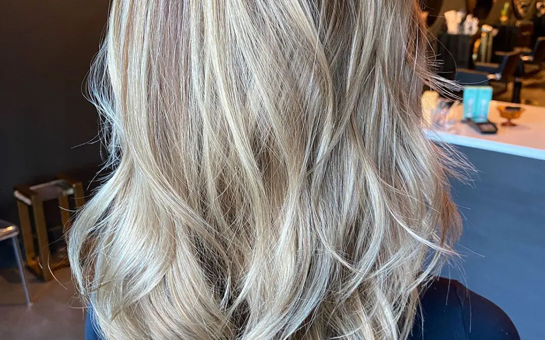 Back view of medium-long hair featuring a dimensional creamy blonde balayage over a sandy base, styled in soft piecey waves by Lisa Edwards at Sunday Salon in Raleigh, NC.
