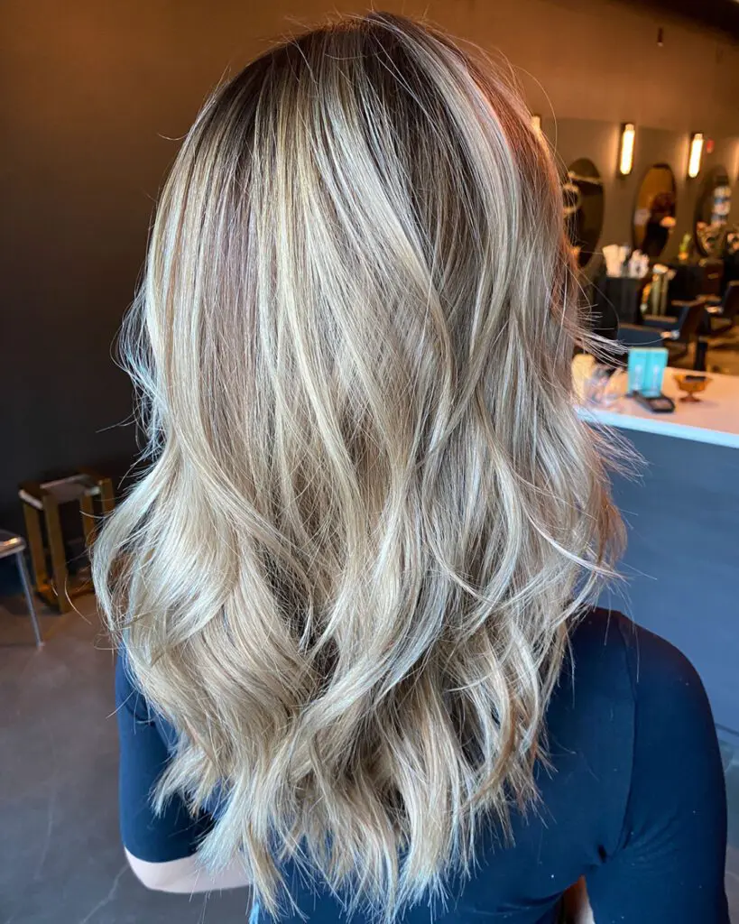 Back view of medium-long hair featuring a dimensional creamy blonde balayage over a sandy base, styled in soft piecey waves by Lisa Edwards at Sunday Salon in Raleigh, NC.