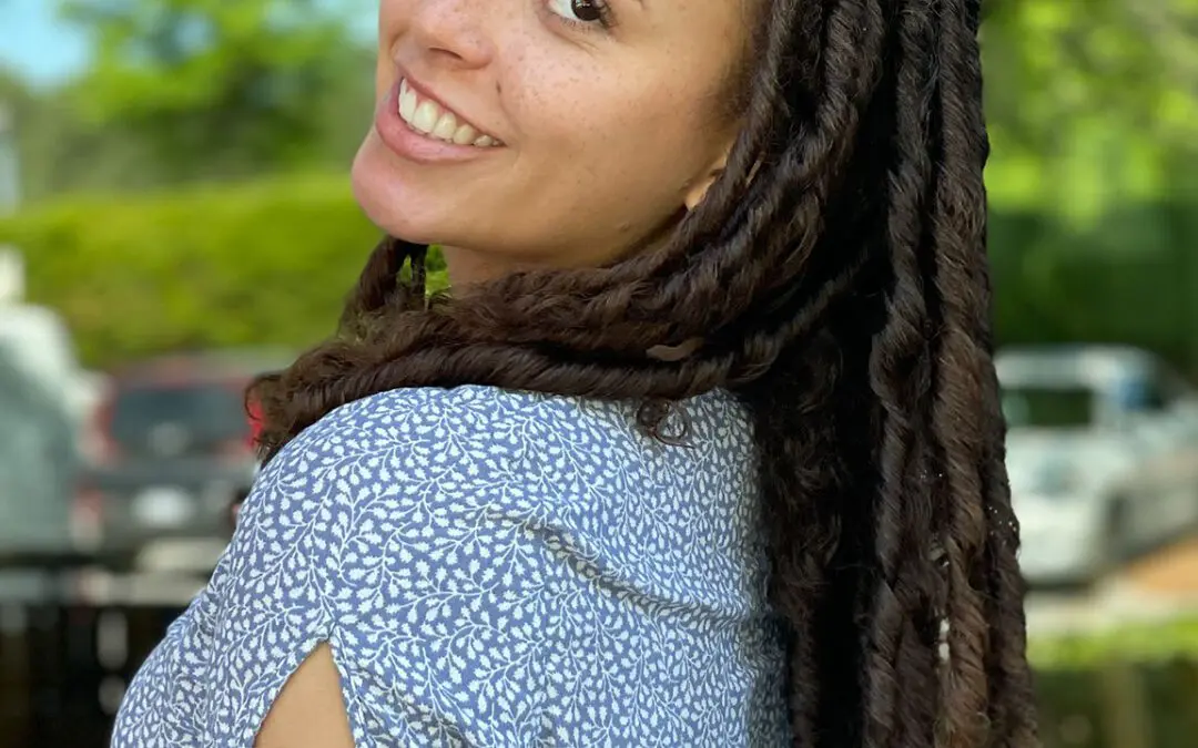 A smiling woman looking over her shoulder showcasing long, thick natural hair styled in beautifully defined deep brunette two-strand twists by a curly hair specialist at Sunday Salon in Raleigh, NC.