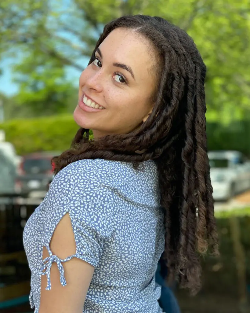 A smiling woman looking over her shoulder showcasing long, thick natural hair styled in beautifully defined deep brunette two-strand twists by a curly hair specialist at Sunday Salon in Raleigh, NC.
