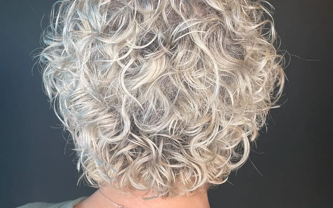 Back view of a voluminous short curly haircut showcasing tight icy blonde ringlets and a dimensional shadow root, created by a curly hair stylist at Sunday Salon in Raleigh, NC.