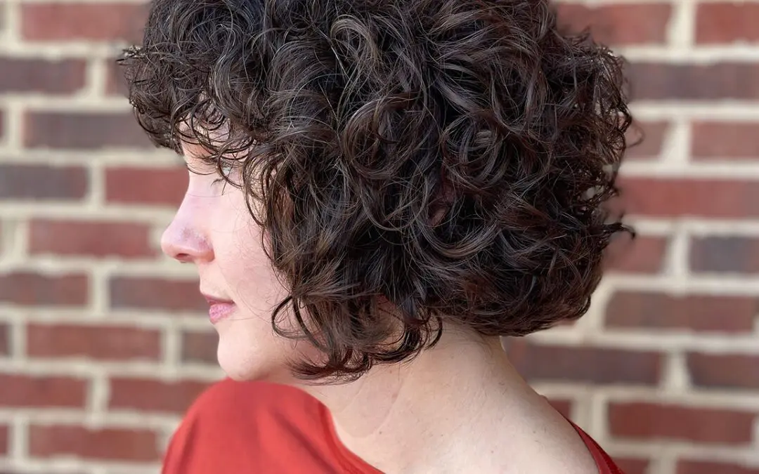 Side profile of a woman with a voluminous, chin-length dark espresso brunette curly bob haircut showcasing perfectly defined natural ringlets, styled at Sunday Salon in Raleigh, NC.