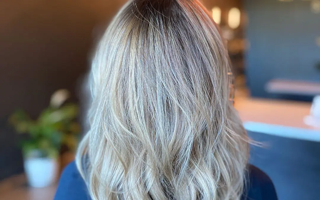 Back view of a woman inside a salon with long, wavy icy ash blonde hair featuring bright dimensional highlights and a dark shadow root by Lisa Edwards at Sunday Salon in Raleigh, NC.