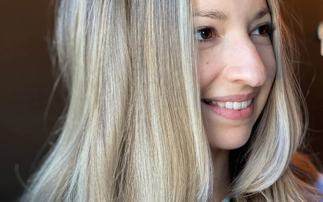 Smiling woman with medium-long straight hair featuring high-contrast vanilla blonde highlights, a seamless shadow root, and sleek face-framing layers, styled at Sunday Salon in Raleigh, NC.
