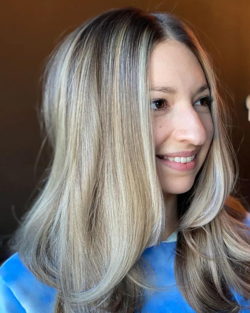 Smiling woman with medium-long straight hair featuring high-contrast vanilla blonde highlights, a seamless shadow root, and sleek face-framing layers, styled at Sunday Salon in Raleigh, NC.