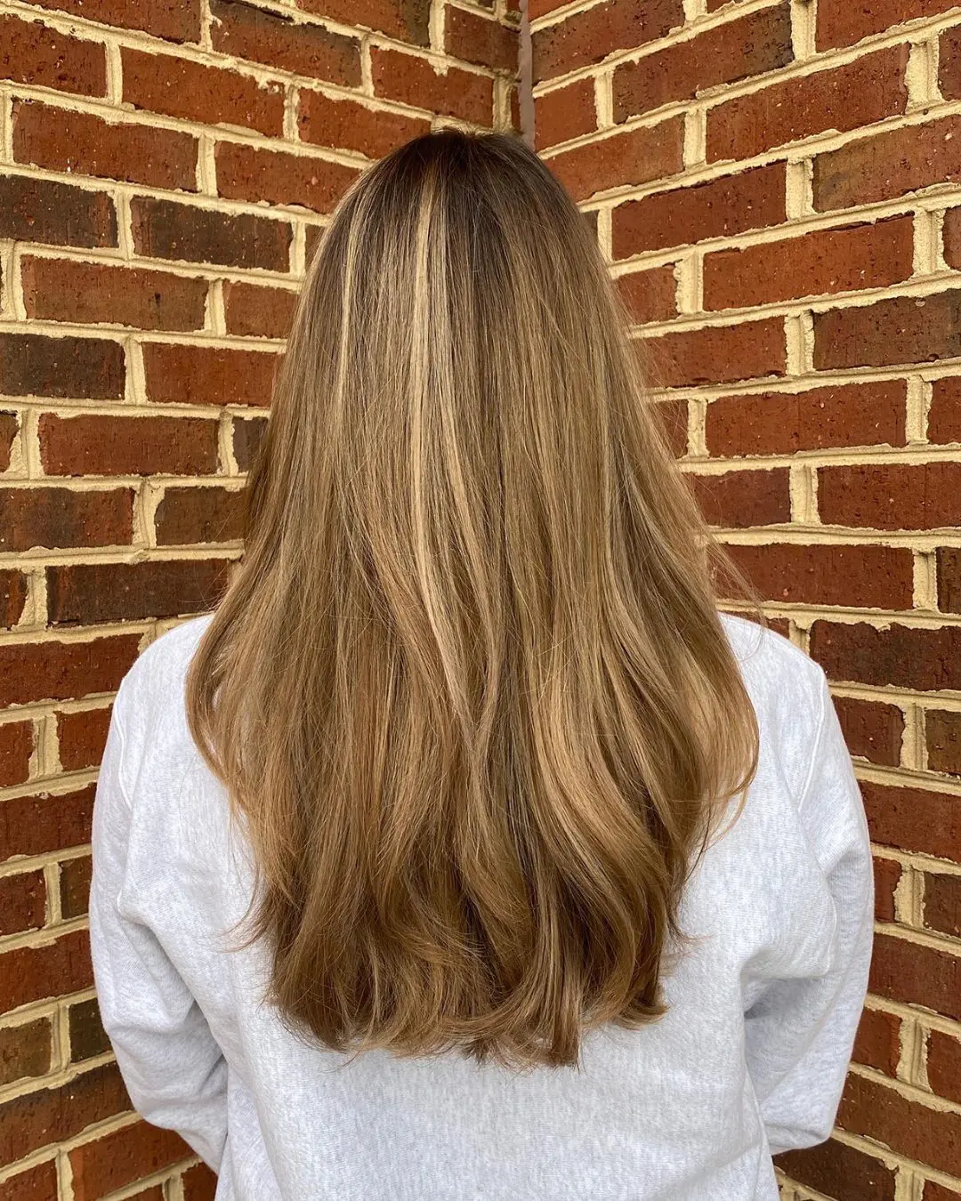 Back view of a woman with ultra-long, thick light brown hair featuring bright golden blonde highlights and a smooth blowout styling at Sunday Salon in Raleigh, NC.