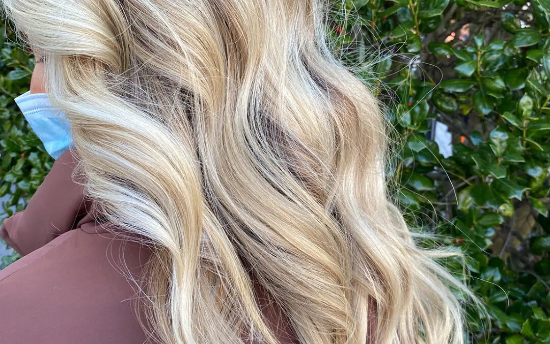 Profile view of a woman outdoors with ultra-long, thick wavy hair featuring bright creamy blonde highlights and a shadow root by Lisa Edwards at Sunday Salon in Raleigh, NC.
