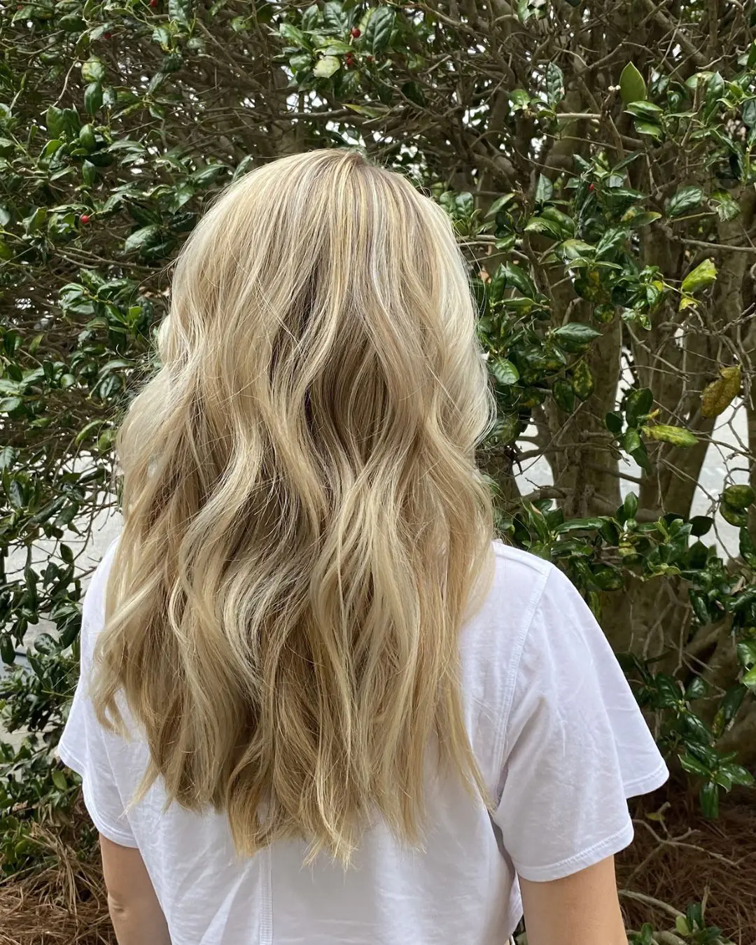 Bright Creamy Blonde Highlights with Beachy Waves and a Soft Shadow Root Back view of a woman outdoors with long wavy hair featuring bright creamy blonde highlights and a soft shadow root by Sunday Salon in Raleigh, NC.