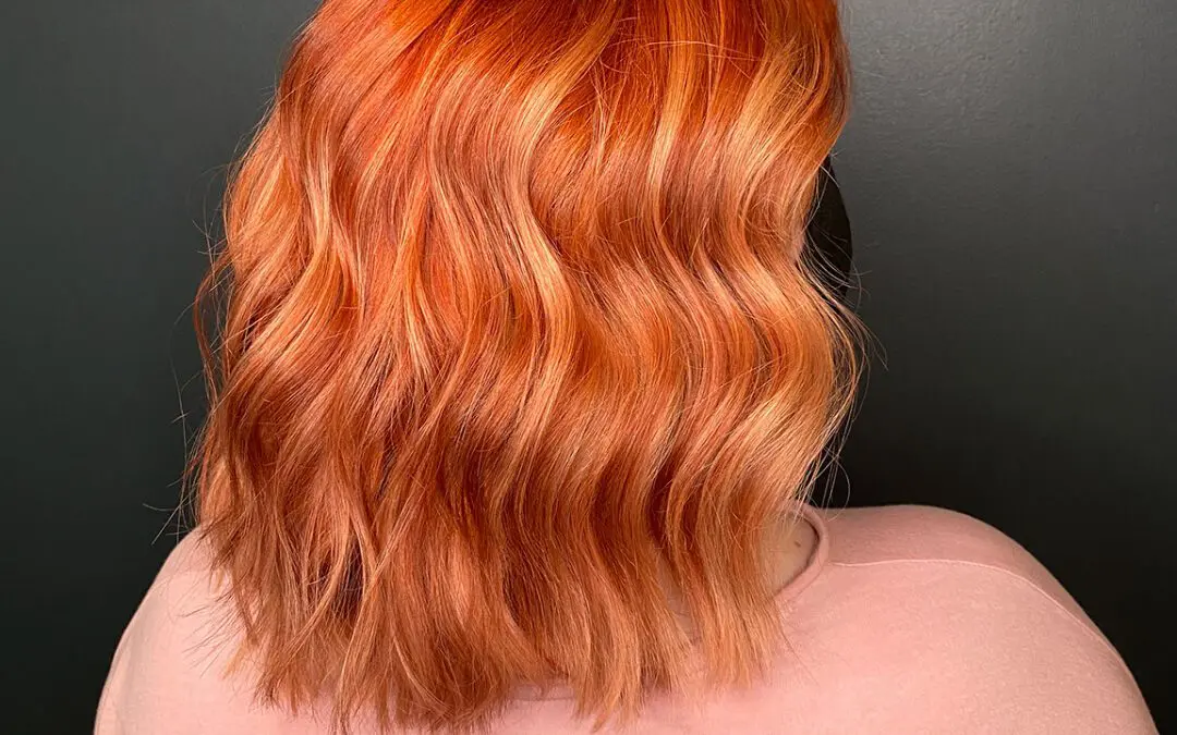Back view of a woman with a collarbone-length blunt lob featuring a vibrant, vivid fiery orange and copper custom color styled in soft waves at Sunday Salon in Raleigh, NC.