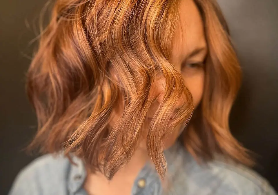 A woman with a textured, wavy long bob haircut featuring a warm, dimensional Cowboy Copper custom color by Lisa Edwards at Sunday Salon in Raleigh, NC.