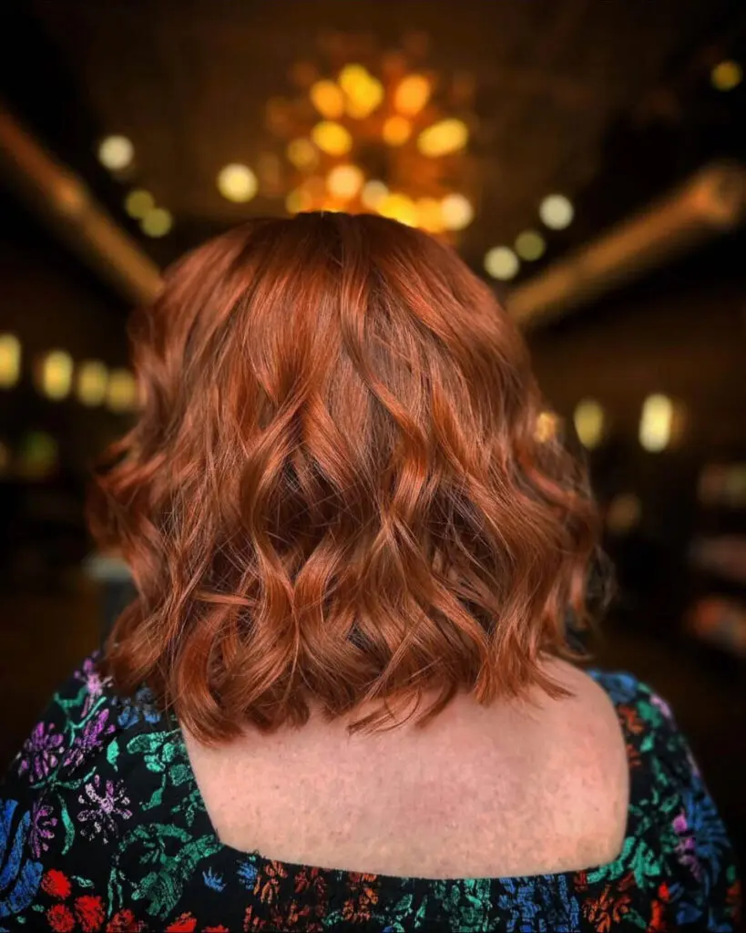 Dimensional Ruby and Fiery Copper Lob with Textured Waves Back view of a woman with a textured wavy lob haircut featuring a vibrant, multi-dimensional ruby and copper custom color by Lisa Edwards at Sunday Salon in Raleigh, NC.