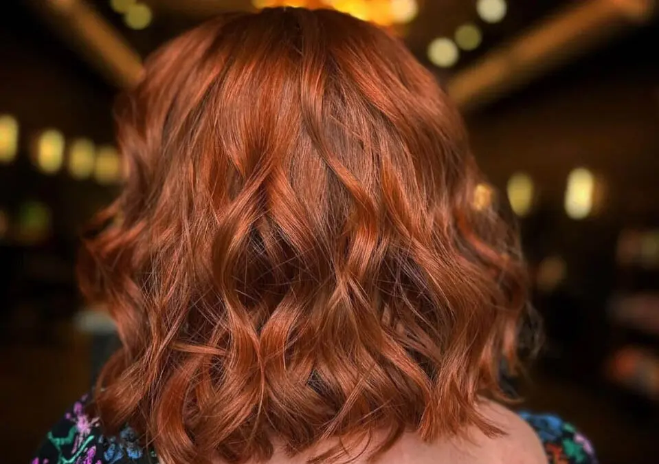 Back view of a woman with a textured wavy lob haircut featuring a vibrant, multi-dimensional ruby and copper custom color by Lisa Edwards at Sunday Salon in Raleigh, NC.