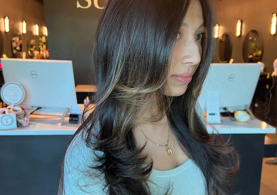 Woman showcasing long, dark brunette hair styled with voluminous sweeping layers and a high-contrast blonde face-framing money piece, custom colored by Lizzie Post at Sunday Salon in Raleigh, NC.