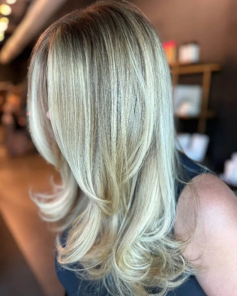 Side profile of a woman with medium-long, smooth hair featuring finely woven icy vanilla blonde highlights, a subtle shadow root, and bouncy layered ends, custom colored by Lizzie Post at Sunday Salon in Raleigh, NC.
