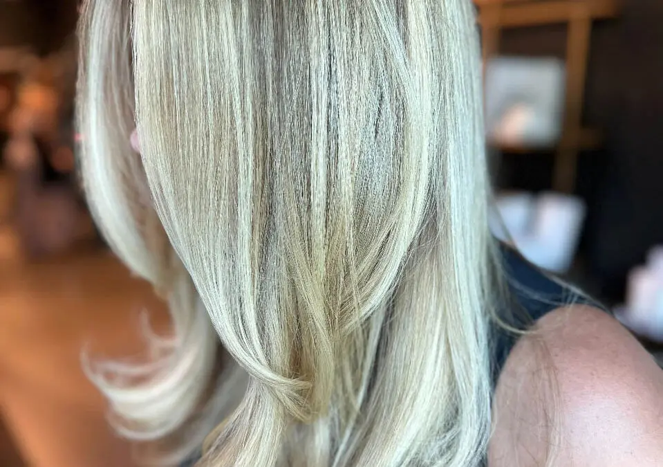 Side profile of a woman with medium-long, smooth hair featuring finely woven icy vanilla blonde highlights, a subtle shadow root, and bouncy layered ends, custom colored by Lizzie Post at Sunday Salon in Raleigh, NC.