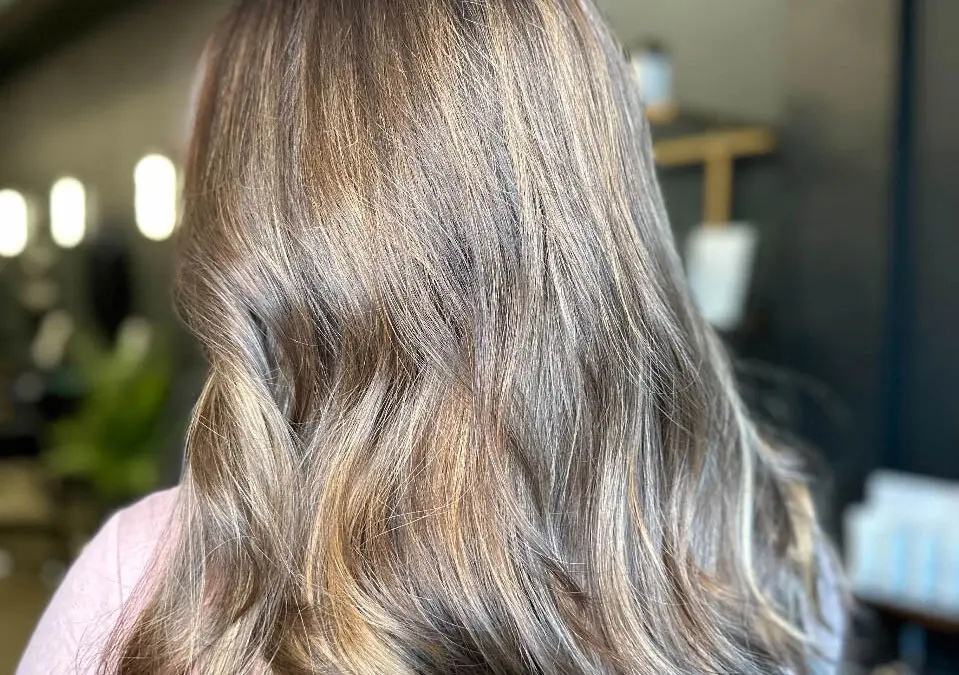 Back view of a woman with medium-long hair featuring a dimensional honey and caramel bronde balayage styled in soft sweeping waves, custom colored by Lizzie Post at Sunday Salon in Raleigh, NC.