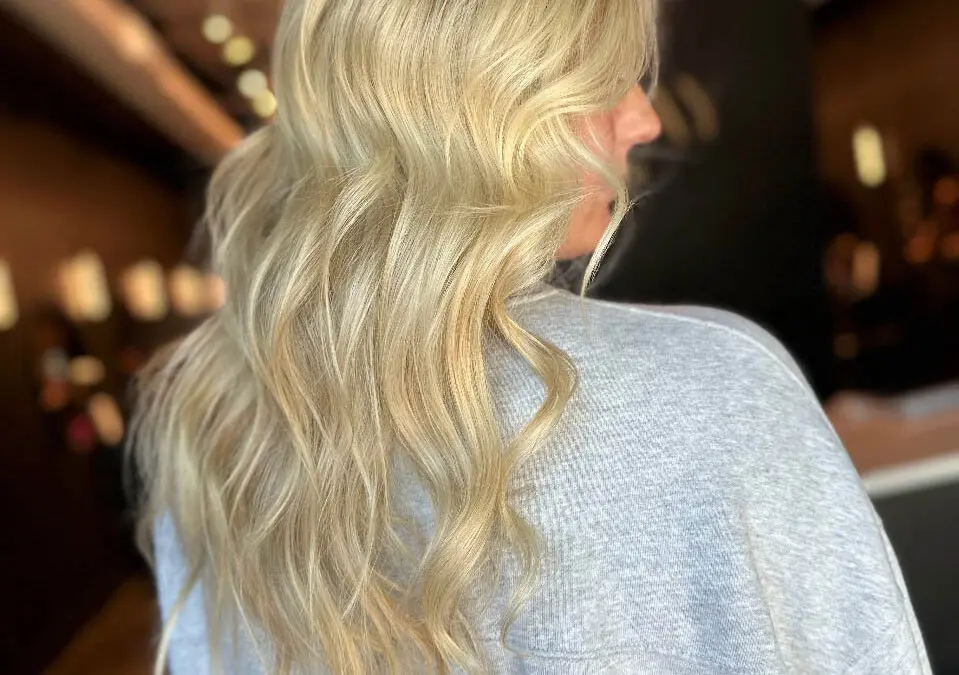 Back view of a woman with long, radiant buttery blonde hair styled in soft cascading waves, featuring a seamless custom color application by Lizzie Post at Sunday Salon in Raleigh, NC.