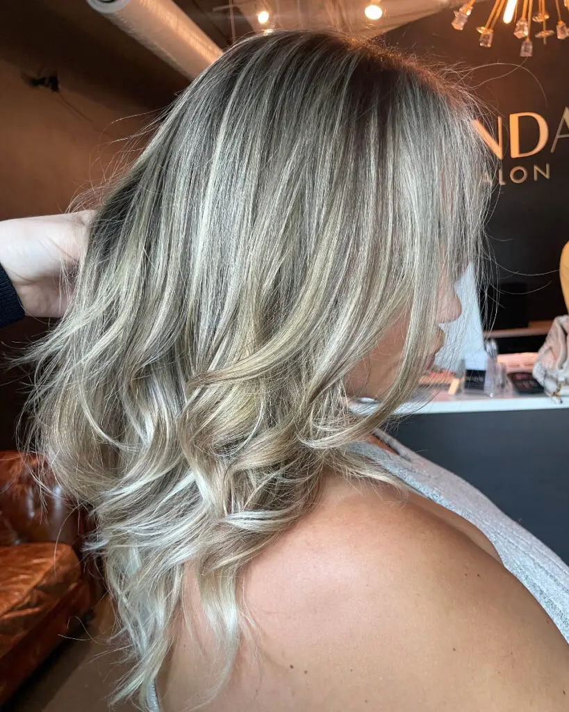 Dimensional Icy Vanilla and Ash Blonde Balayage with Textured Layers Side profile of a woman with medium-length textured layered hair showcasing a high-contrast icy vanilla and ash blonde balayage, custom colored by Lizzie Post at Sunday Salon in Raleigh, NC.