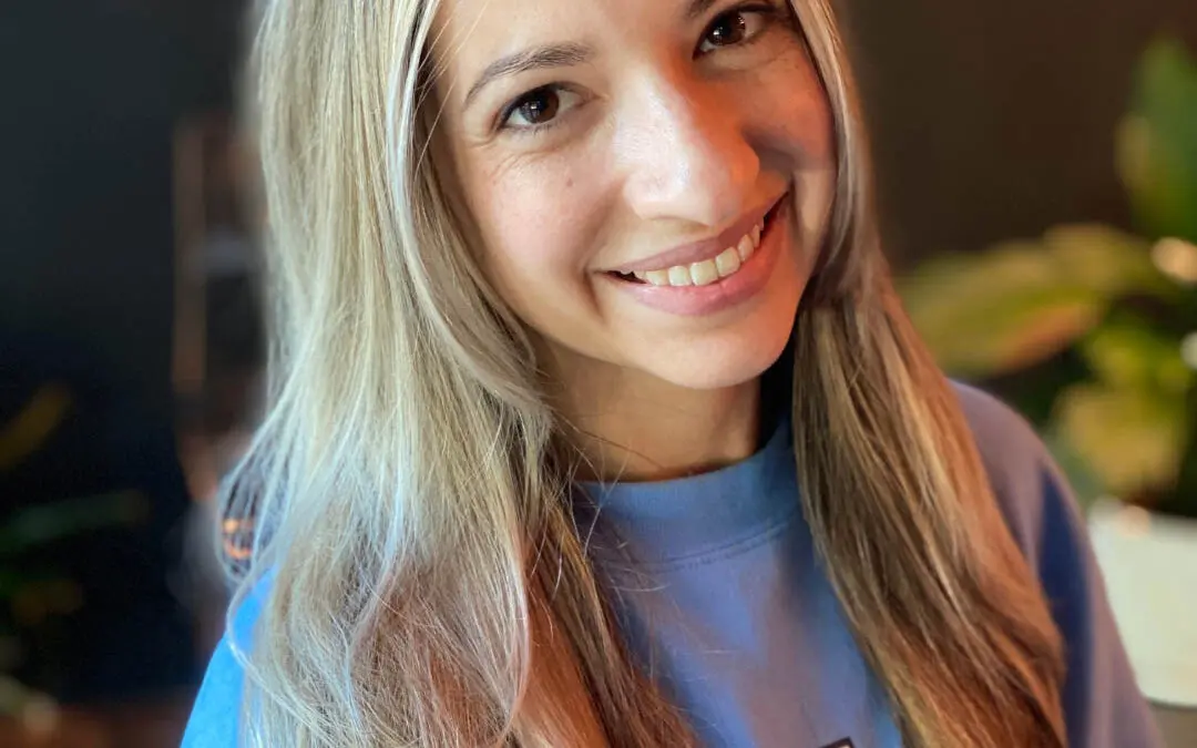 Close-up photo of a smiling client showcasing long sleek bronde hair with bright blonde face-framing highlights and a shadow root, custom colored by Lisa Edwards at Sunday Salon in Raleigh, NC.