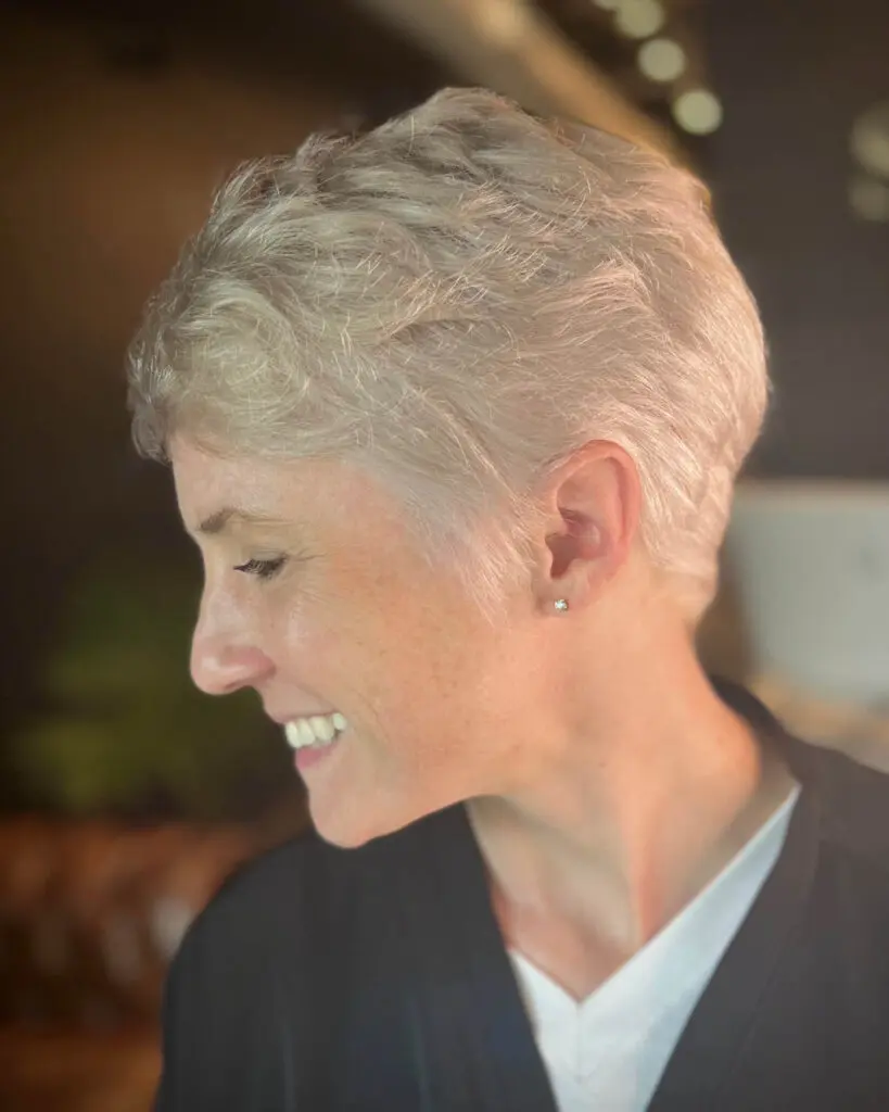 Side profile photograph of a smiling client showcasing a short, cool-toned silver pixie cut with a clean taper on the back and defined texture on top, created by Katherine Beingolea at Sunday Salon in Raleigh, NC.
