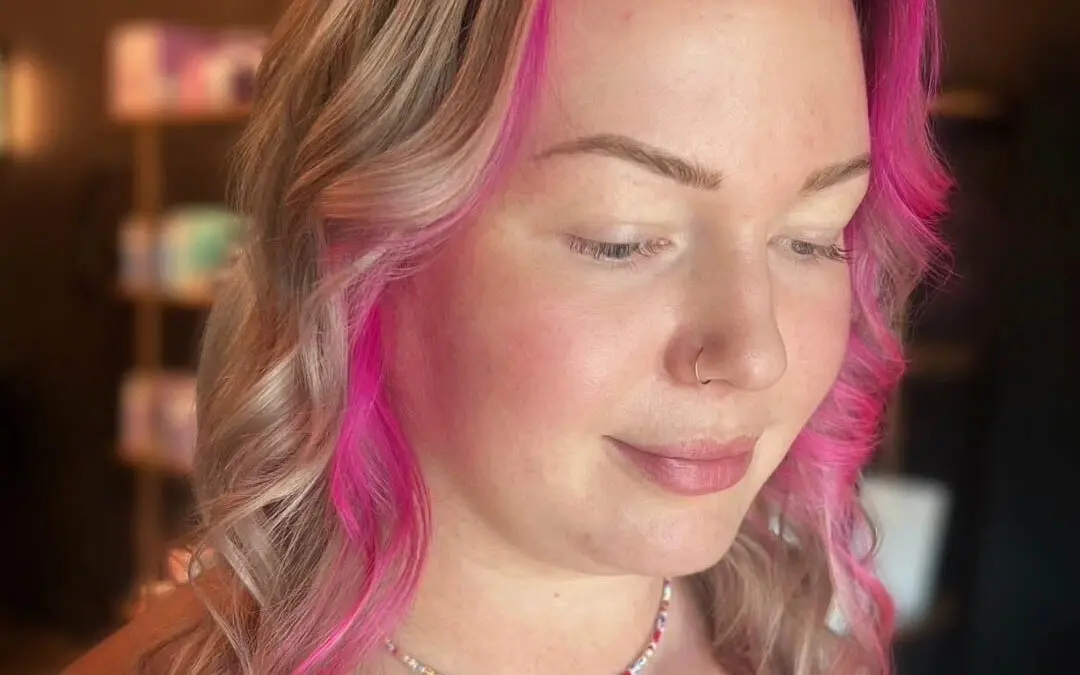 Close-up photo of a client with shoulder-length ash blonde hair featuring a bold vivid hot pink money piece and face-framing layers styled in soft waves at Sunday Salon in Raleigh, NC.