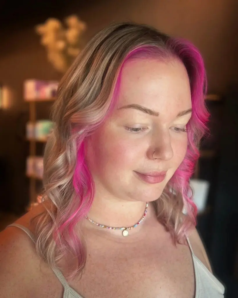 Bold Vivid Pink Face-Framing Color Block with Ash Blonde Waves Close-up photo of a client with shoulder-length ash blonde hair featuring a bold vivid hot pink money piece and face-framing layers styled in soft waves at Sunday Salon in Raleigh, NC.
