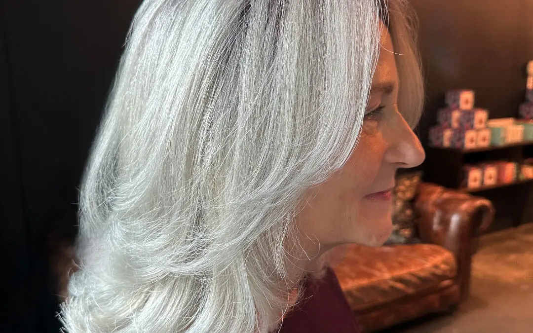 Side profile of a smiling client with elegant, glossy icy silver hair styled in a sweeping layered blowout at Sunday Salon in Raleigh, NC.
