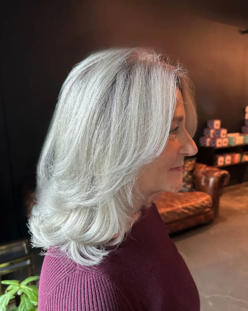 Side profile of a smiling client with elegant, glossy icy silver hair styled in a sweeping layered blowout at Sunday Salon in Raleigh, NC.