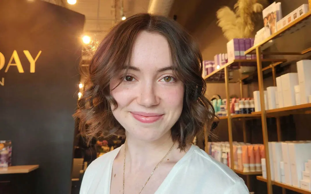 Smiling client showing off a chin-length dark chocolate brunette bob styled with soft, loose waves by Jess Mallard at Sunday Salon in Raleigh, NC.