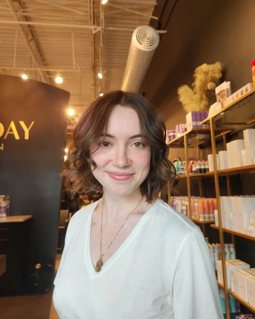 Smiling client showing off a chin-length dark chocolate brunette bob styled with soft, loose waves by Jess Mallard at Sunday Salon in Raleigh, NC.