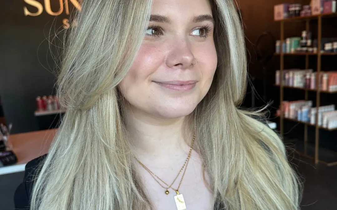 Smiling woman with long, voluminous hair featuring a bright vanilla blonde balayage, a bold money piece, and swooping face-framing layers, custom colored by Lisa Edwards at Sunday Salon in Raleigh, NC.