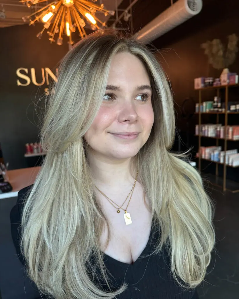 Bright Vanilla Blonde Balayage with Voluminous Face-Framing Layers Smiling woman with long, voluminous hair featuring a bright vanilla blonde balayage, a bold money piece, and swooping face-framing layers, custom colored by Lisa Edwards at Sunday Salon in Raleigh, NC.