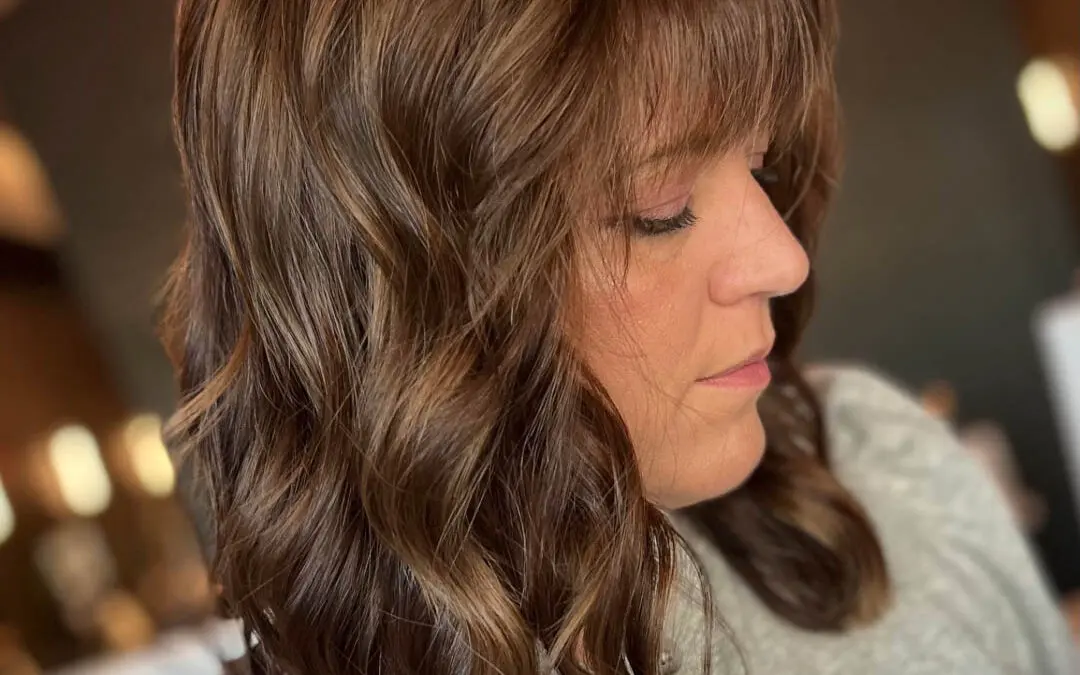 Side profile of a client with a dimensional chocolate brunette lob, wispy bangs, and subtle caramel highlights styled in soft waves by Katherine Beingolea at Sunday Salon in Raleigh, NC.