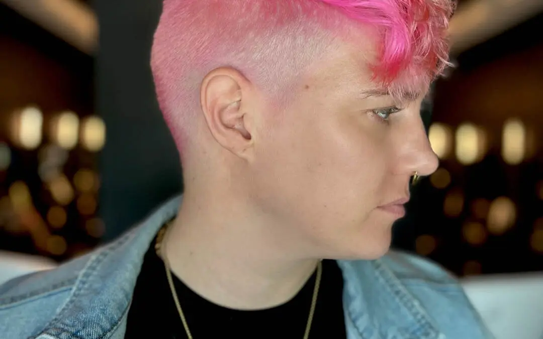 Side profile of a client showcasing a bold neon pink hair color with a clipper-faded undercut and longer textured waves on top, created by Katherine Beingolea at Sunday Salon in Raleigh, NC.