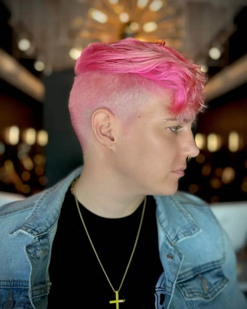 Side profile of a client showcasing a bold neon pink hair color with a clipper-faded undercut and longer textured waves on top, created by Katherine Beingolea at Sunday Salon in Raleigh, NC.