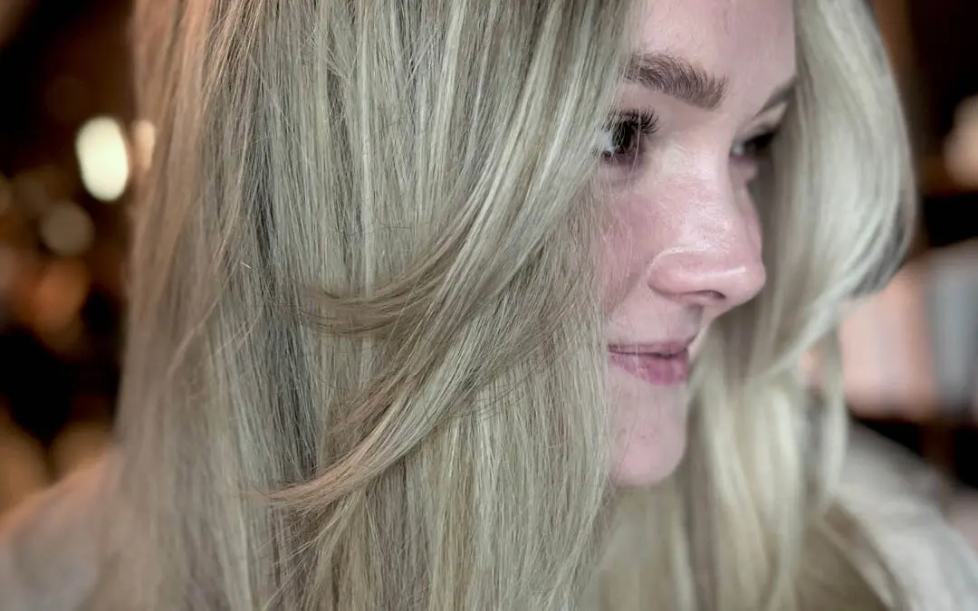 Side profile of a smiling client with long creamy champagne blonde hair and sweeping face-framing layers, custom cut and colored by Katherine Beingolea at Sunday Salon in Raleigh, NC.