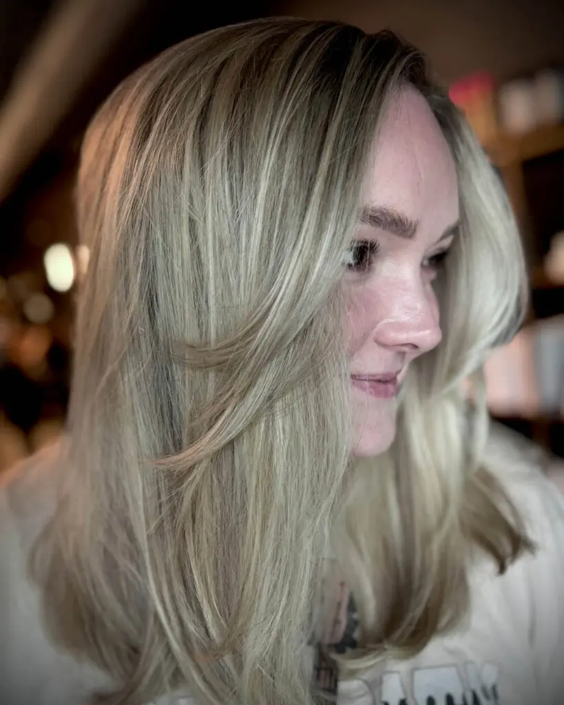 Side profile of a smiling client with long creamy champagne blonde hair and sweeping face-framing layers, custom cut and colored by Katherine Beingolea at Sunday Salon in Raleigh, NC.
