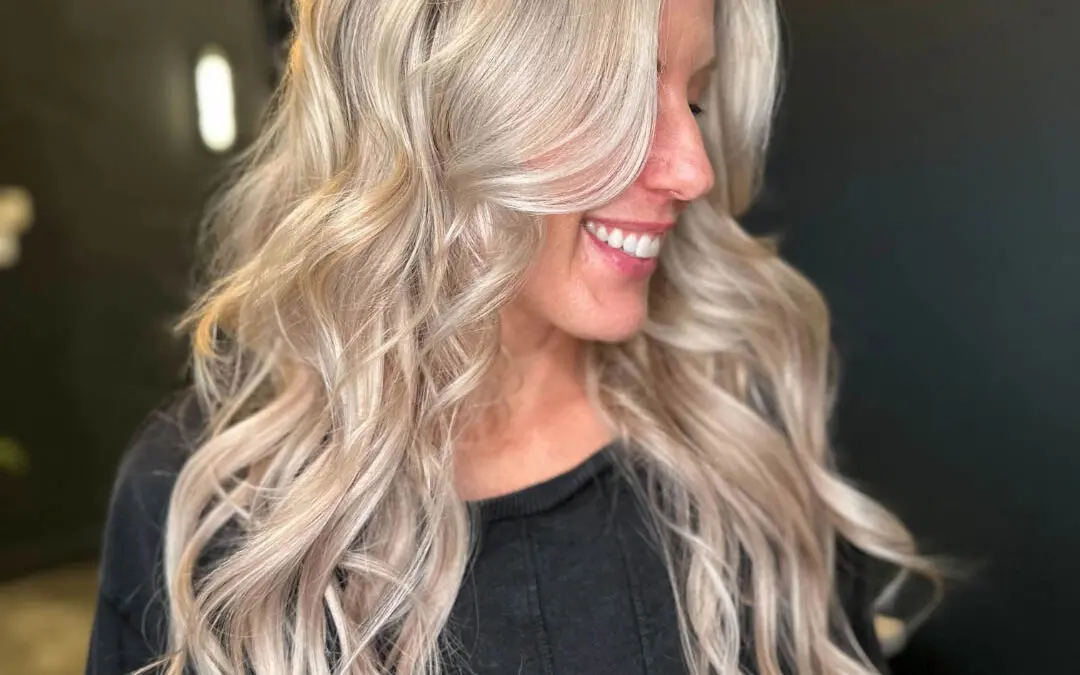 Side profile of a smiling client with very long, icy pearl blonde hair styled in voluminous beachy waves and sweeping face-framing layers at Sunday Salon in Raleigh, NC.