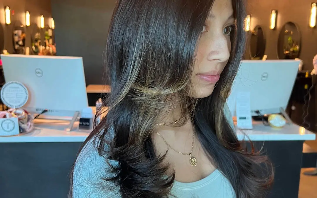 Side profile of a client with ultra-long dark brunette hair, heavy bouncy layers, and high-contrast blonde face-framing highlights styled in a voluminous blowout at Sunday Salon in Raleigh, NC.