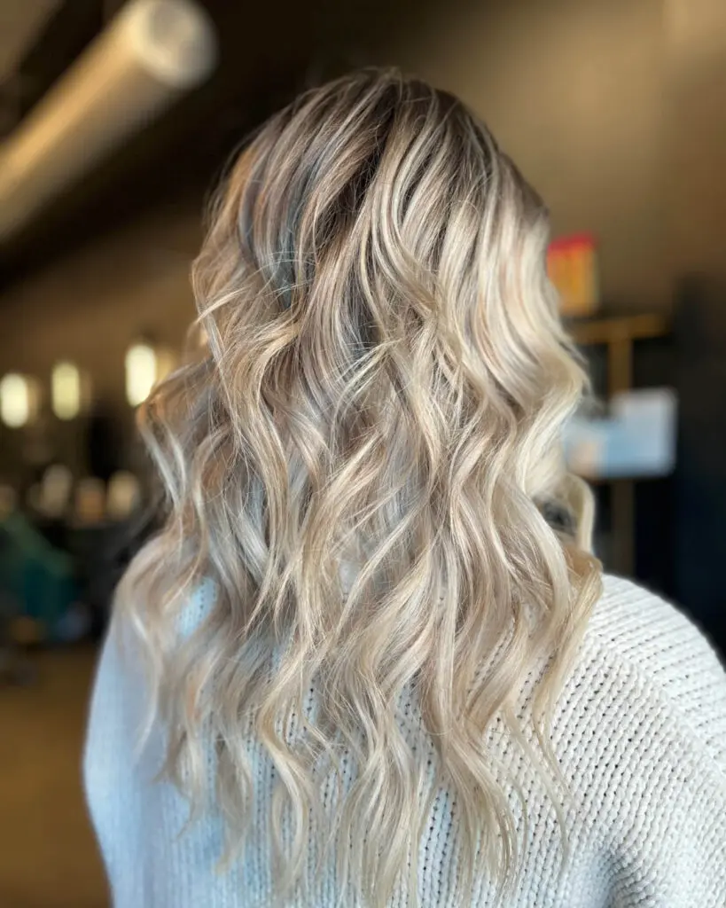 Back view of a client showcasing long dimensional vanilla and icy blonde balayage hair with a shadow root, styled in piecey beachy waves at Sunday Salon in Raleigh, NC.